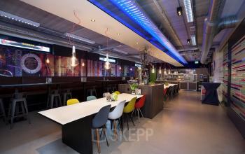 Kantoorruimte huren op Europalaan 24 in Maastricht-Airport. Moderne gemeubileerde werkruimte met lange tafel en gekleurde stoelen, geschikt voor vergaderen en samenwerken.