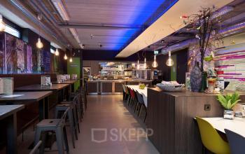 Kantine met moderne meubels, hoge tafels, gekleurde stoelen en hanglampen in kantoorpand aan Europalaan 24, Maastricht-Airport.