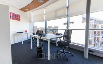 Lichte kantoorruimte huren op Avenue Ceramique 221 in Maastricht met grote ramen, enkele bureaus en stoelen, geschikt voor werk en samenwerking.