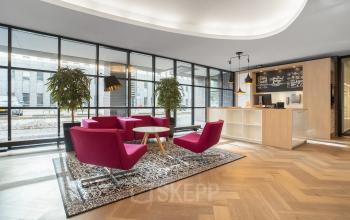 Moderne kantoorruimte met roze stoelen, een tapijt en een balie, geschikt voor kantoorruimte huren in Maastricht.