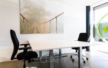 Moderne kantoorruimte in Made met twee bureaustoelen en een groot raam dat natuurlijk licht biedt. Ideale plek voor productief werken. Decoratieve wandkunst voegt een creatieve touch toe.