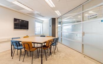 Kantoorruimte huren in Meppel bij Blankenstein 265, met een vergadertafel, kleurrijke stoelen en een flatscreen. Heldere verlichting en glazen wanden geven een moderne uitstraling.