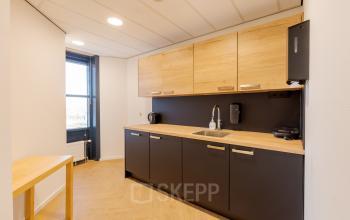 Moderne pantry in een kantoorpand op Blankenstein 265 te Meppel, met houten kastdeuren, een strak aanrecht en ingebouwde spoelbak. Ideale ruimte voor ontspanning op de werkplek.