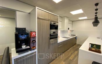 Moderne pantry met houten kasten, koffiezetapparaat, oven en magnetron in kantoorpand aan Rijksweg 79, Naarden.