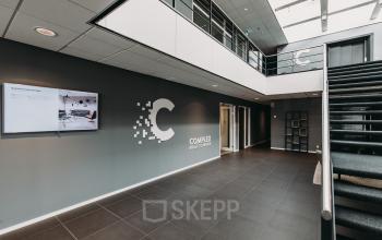 Kantoorpand aan de Rijksweg 79 in Naarden met een moderne entree, trap naar de eerste verdieping en een groot logo van het complex op de muur.