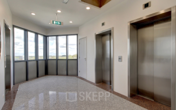 Entree van kantoorpand Nevelgaarde 8-35 in Nieuwegein met twee liften en uitzicht op de omgeving, ideaal voor bedrijven die kantoorruimte willen huren.