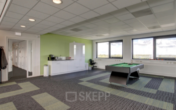 Lichte en ruime kantoorruimte huren aan Nevelgaarde 8-35 in Nieuwegein, met grote ramen en een modern interieur. Voorzien van vloerbedekking met patroon en een speelse tafeltennis-tafel, ideaal voor creatieve werkomgevingen.