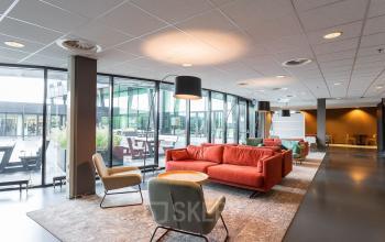 Moderne kantoorruimte te huur in Nijmegen aan Jonkerbosplein 52, met kleurrijk gemeubileerde hoek en grote ramen voor veel natuurlijk licht.