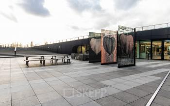 Exterieur van kantoorpand op Jonkerbosplein 52 in Nijmegen, met groot terras en glazen kunstwerk. Perfecte ruimte voor wie overweegt kantoorruimte te huren.