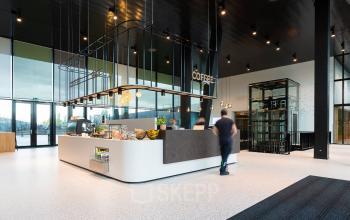 Moderne kantoorruimte met een koffiebar in het kantoorpand op Jonkerbosplein 52, Nijmegen. Mensen bestellen koffie, wat de werkplek levendig maakt. Optioneel voor kantoorruimte huren.