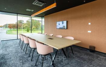 Vergaderruimte in kantoorpand op Jonkerbosplein 52, Nijmegen, met grote tafel omringd door stoelen, uitkijkend op groene omgeving. Ideaal voor bedrijven die kantoorruimte willen huren.
