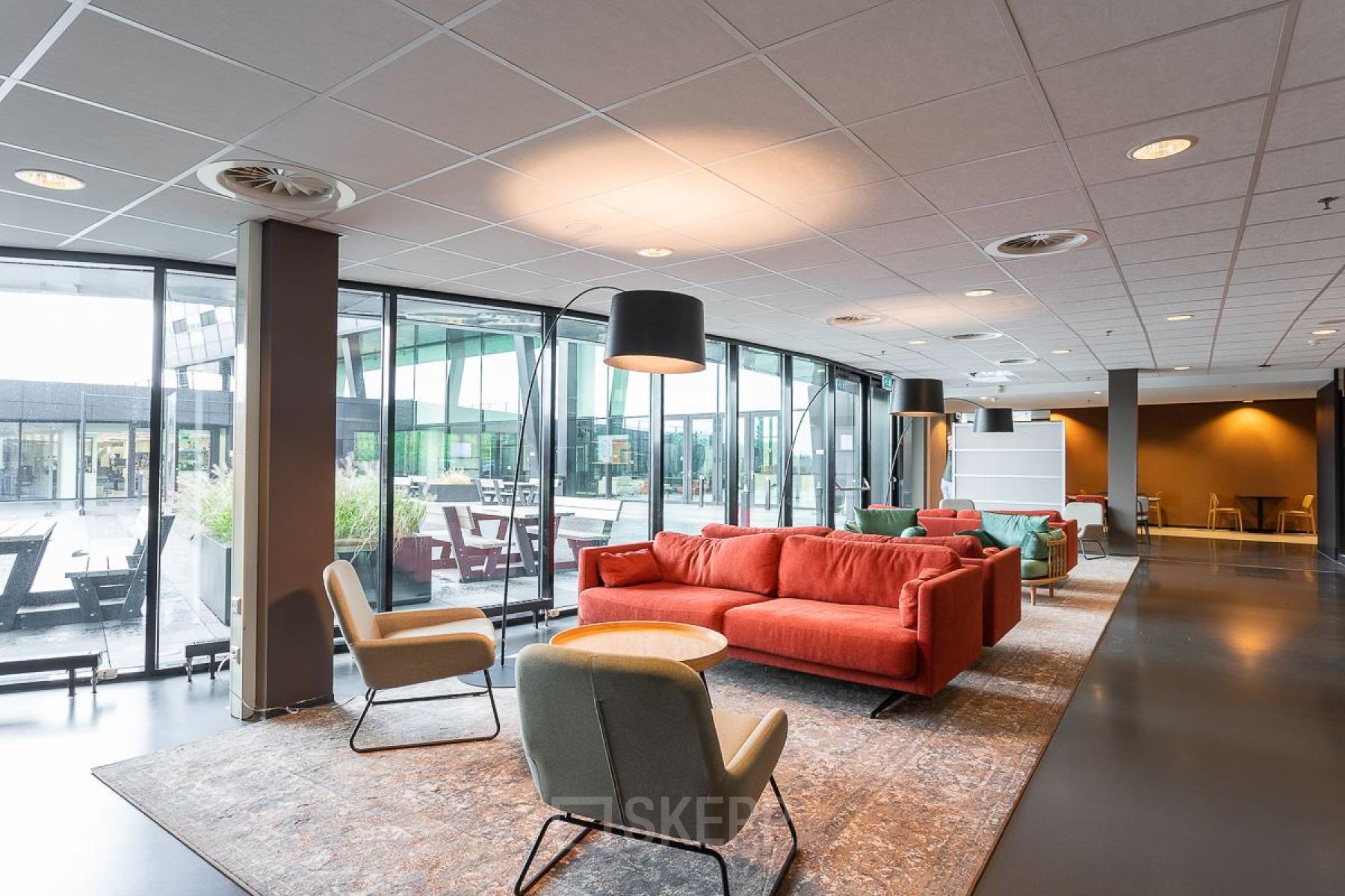 Moderne kantoorruimte in Nijmegen met comfortabele zithoek, ingericht met een rode bank en accentstoelen, gelegen aan het Jonkerbosplein 52.