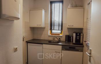 Compacte pantry met witte kasten, een gootsteen en een koffiezetapparaat in kantoorpand op Abdis van Thornstraat 74, Oosterhout Nb. Ideaal voor bedrijven die kantoorruimte huren en een functionele keuken wensen.