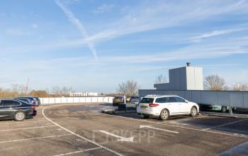 Parkeerplaats bij kantoorpand op Veengang 1 in Oosterwolde met meerdere geparkeerde auto's onder een blauwe lucht.