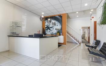 Een lichte en moderne receptie van een kantoorpand op Leeghwaterstraat 25, Reeuwijk. Er staat een bureau met een medewerker bezig met administratieve taken. Kantoorruimte huren is hier mogelijk.