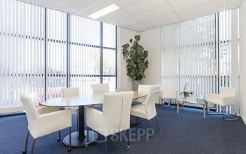 Moderne kantoorruimte te huren op Leeghwaterstraat 25, Reeuwijk, met witte stoelen rondom een ronde tafel en grote ramen met verticale jaloezieën.