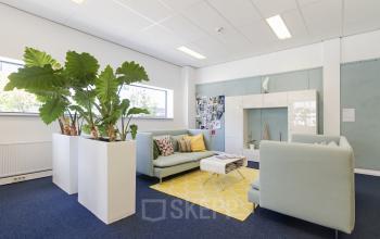 Heldere kantoorruimte op Leeghwaterstraat 25 in Reeuwijk, met groene planten, comfortabele banken en een kleurrijk kleed, ideaal voor een lounge of informele bespreking.