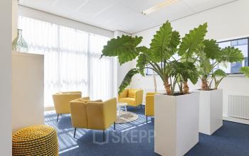 Kantoorruimte huren aan de Leeghwaterstraat 25 in Reeuwijk. Ruimte met blauwe vloerbedekking, gele stoelen, grote planten en veel natuurlijk licht.