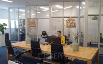 Kantoorruimte op Leeghwaterstraat 25 in Reeuwijk met houten tafel en stoelen, raamwerk en decoratieve elementen. Persoon werkt aan een bureau. Ideale plek om een kantoor te huren.