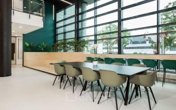 Kantoorruimte huren in kantoorpand op Einsteinlaan 28, Rijswijk met moderne werkplekken en grote ramen. Groen meubilair en planten geven de ruimte een frisse uitstraling.