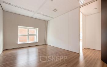 Lege kantoorruimte op Laan van Vredenoord 17-19 in Rijswijk met houten vloer en raam, ideaal voor huren als kantoorpand.
