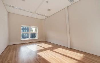 Lichte, lege kantoorruimte met houten vloer en groot raam in kantoorpand aan Laan van Vredenoord 17-19, Rijswijk.