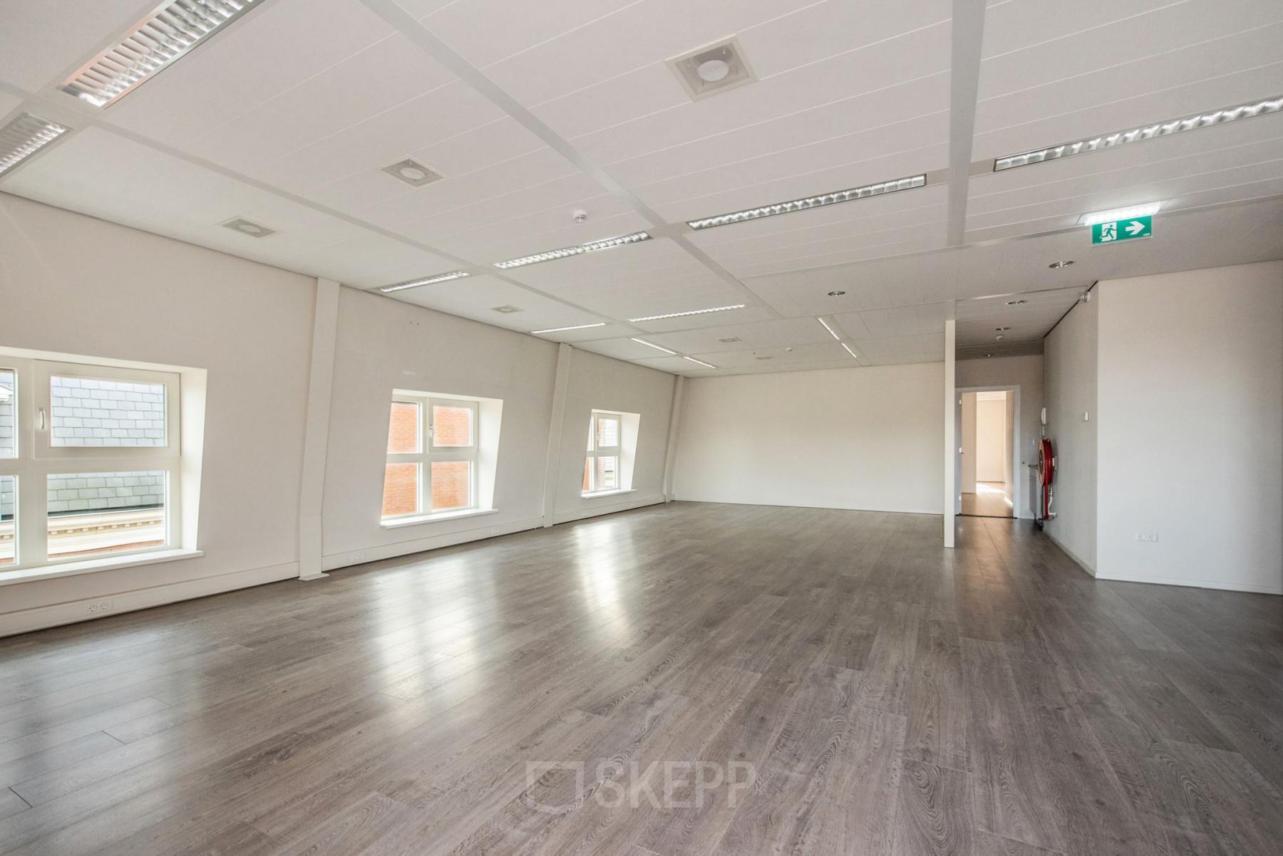 Lichte, ongemeubileerde kantoorruimte met houten vloer en grote ramen aan de Laan van Vredenoord 17-19 in Rijswijk, ideaal voor kantoorruimte huren.