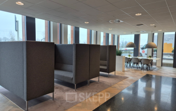 Moderne lounge in het kantoorpand op Laan van Zuid Hoorn 70, Rijswijk, met grijze zitbanken en grote ramen. Een stijlvolle plek voor kantoorruimte huren.