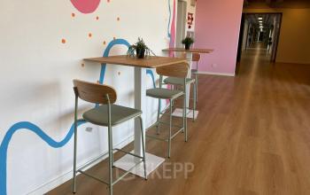 Interieurfoto van kantoorpand aan Generaal Eisenhowerplein 111 111, Rijswijk met hoge stoelen en tafels bij een kleurrijk beschilderde muur, geschikt voor creatief werken of informele meetings.