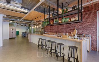Stijlvol ingerichte kantoorruimte op Patrijsweg 62 te Rijswijk met een moderne bar en hoge krukken tegen een bakstenen muur. Geschikt voor huur als kantoor of vergaderruimte.