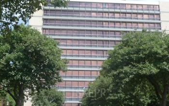 Voorzijde van een kantoorgebouw gelegen aan J.C. van Markenlaan 3 in Rijswijk, omgeven door bomen en een parkeerruimte aan de voorkant.