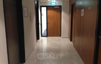 Een smalle gang in een kantoorpand op JC van Markenlaan 3, Rijswijk, met marmeren vloer en houten deuren. Ideaal voor kantoorruimte huren.