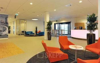 Moderne lobby met kleurrijke meubels in het kantoorpand gelegen op Patrijsweg 4-140 in Rijswijk. Drie mensen zijn in gesprek bij de receptiebalie.