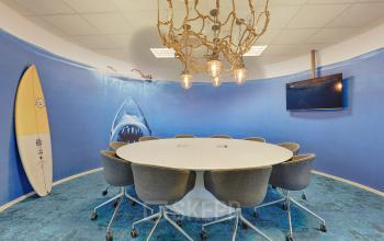 Vergaderruimte in kantoorpand Patrijsweg 4-140, Rijswijk, met ronde tafel, grijze stoelen en muurdecoratie van haai en surfplank.