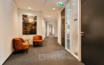 Kantoorpand Kapellerpoort 1 in Roermond, met donkere deuren, verlichte gang en bruin-oranje loungestoelen naast een groot foto-kunstwerk.