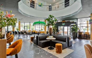 Interieur van modern kantoorpand op Kapellerpoort 1, Roermond, met zitgedeelte, groene planten en bloemen, omgeven door grote ramen.