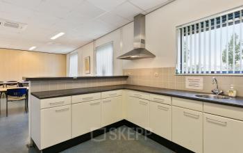 Interieur van kantoorpand Noordhoven 2 in Roermond met een moderne pantry met witte kasten, ventilatiesysteem en uitzicht op een vergaderruimte in de achtergrond, ideaal voor kantoorruimte huren.
