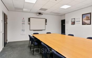 Kantoorruimte huren in Roermond op Noordhoven 2. De foto toont een vergaderruimte met een lange tafel en stoelen, een projector en een whiteboard. Geschikt voor zakelijke bijeenkomsten.