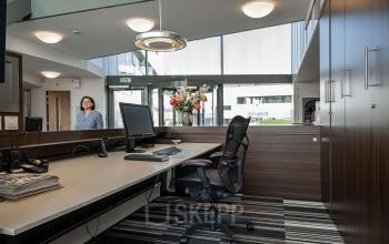 Receptieruimte in een kantoorpand aan Boven de Wolfskuil 3, Roermond, met balie, computerscherm en stoelen. Een persoon staat binnen te kijken vanuit de ingang.