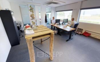 Modern kantoorpand in Roermond met lichte werkplekken, ideaal voor kantoorruimte huren. Twee mensen overleggen aan bureaus. Ruime ramen zorgen voor veel natuurlijk licht.
