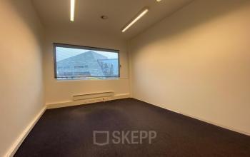 Lege kantoorruimte met grijs tapijt en grote ramen, gelegen in kantoorpand op Boven de Wolfskuil 3, Roermond. Ideaal voor wie kantoorruimte huren overweegt.