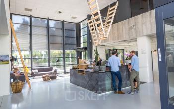 Moderne kantoorlobby met twee personen in gesprek bij een receptiebalie in het kantoorpand aan Marten Meesweg 8-10, Rotterdam Alexander.
