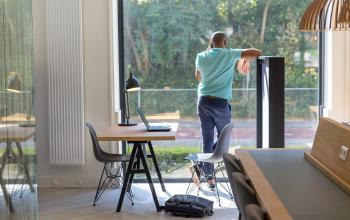 Zakelijke kantoorruimte te huur aan Marten Meesweg 8-10, Rotterdam Alexander, met medewerker die telefoneert naast werkplek met laptop en bureaulamp.