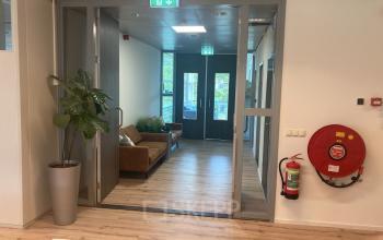 Entree van een kantoorpand aan de Hoofdweg 66 in Rotterdam Alexander, met een brandblusser aan de muur en een glazen deur naar een ontmoetingsruimte met zitbanken.