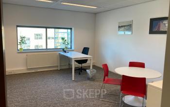 Kantoorruimte huren in Rotterdam Alexander, Hoofdweg 66, met een bureau, een ronde tafel en stoelen, en enkele planten bij het raam.