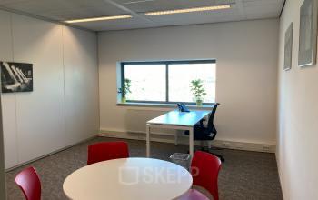 Kantoorruimte huren op Hoofdweg 66, Rotterdam Alexander met een werkplek, tafel met rode stoelen en zicht op een raam.