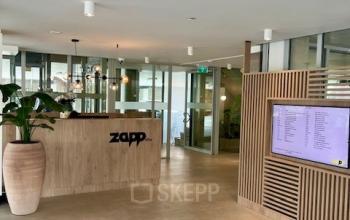 Moderne receptie in kantoorpand aan Bahialaan 100, Rotterdam Brainpark, met grote plantenpot, houten balie en digitaal scherm. Geschikt voor wie kantoorruimte wil huren.