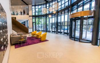 Moderne entree van kantoorpand Weena 290 in Rotterdam Centraal Station met glazen gevel en kleurrijk meubilair.