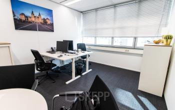 De kantoorruimte op Weena 290, Rotterdam Centraal Station, is licht met grote ramen en afbeeldingen van Rotterdam aan de muur. Er staan bureaus met computers en stoelen, geschikt voor huur.