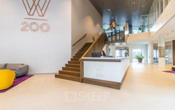 Lichte receptieruimte in kantoorpand Weena 290, Rotterdam Centraal Station, met moderne balie en personen die zakelijke activiteiten uitvoeren. Ideaal voor kantoorruimte huren.